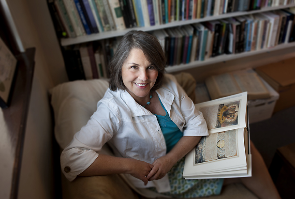 Molly Rothenberg poses in front of full bookshelves with a book open on her lap