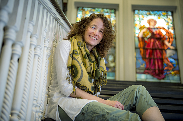 Toni Weiss poses on steps with stained glass windows in the background