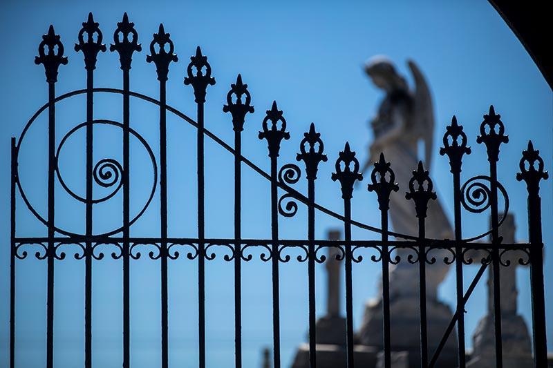 A detailed wrought iron gate guards the entrance to a cemetery in the Upper 9th Ward.