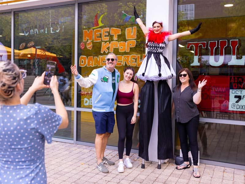 Student Paris Gingold (second from left) and parents Stephen (left) and Renee (right) pose for a picture with a performer on stilts during a circus-themed event.