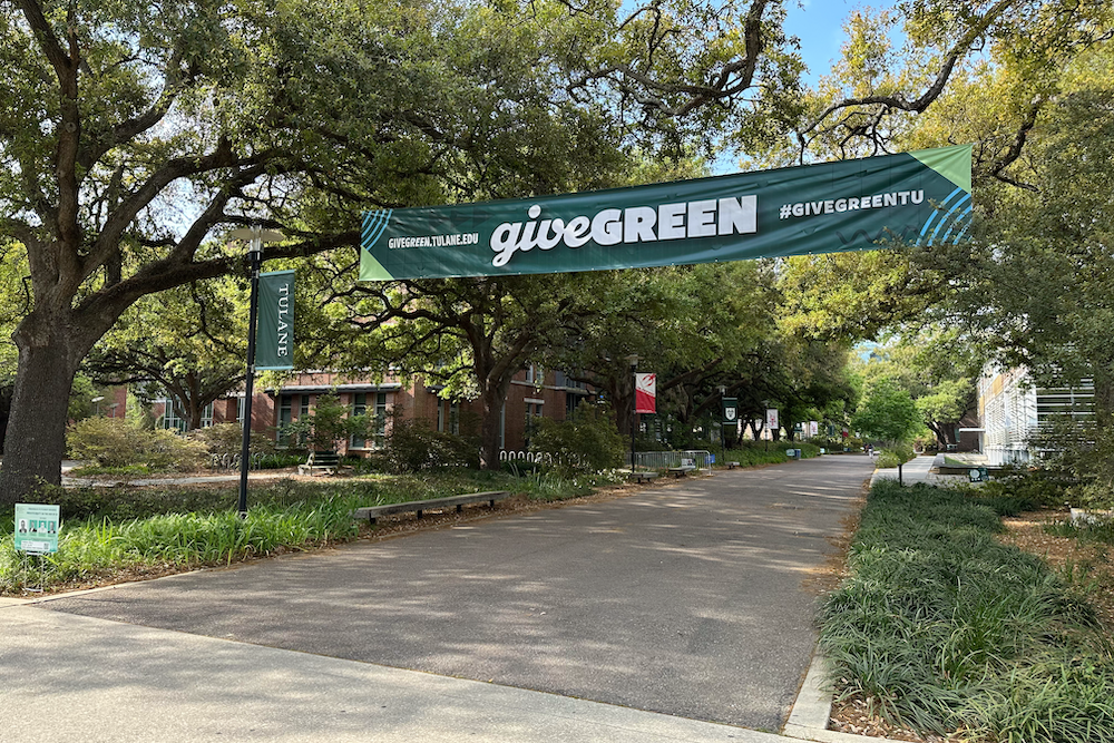 Green "GIVE GREEN" banner hangs across a tree-lined paved path.