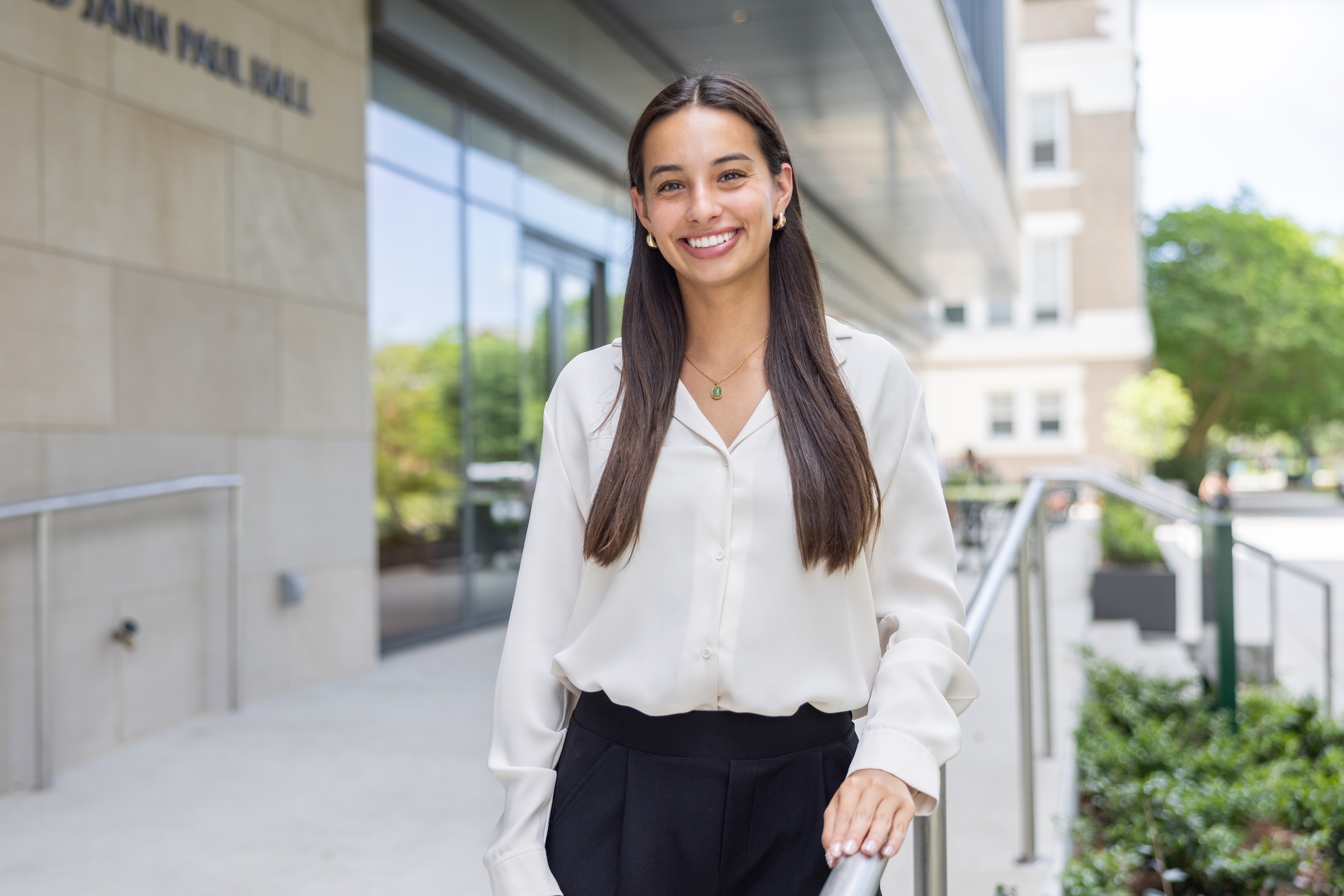 
Smiling young woman in white blouse stands outside modern building. 