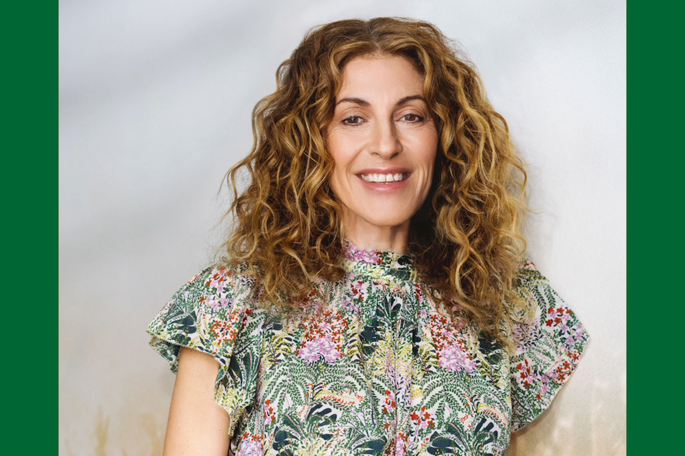 
Smiling woman with long curly brown hair and a colorful floral top. 