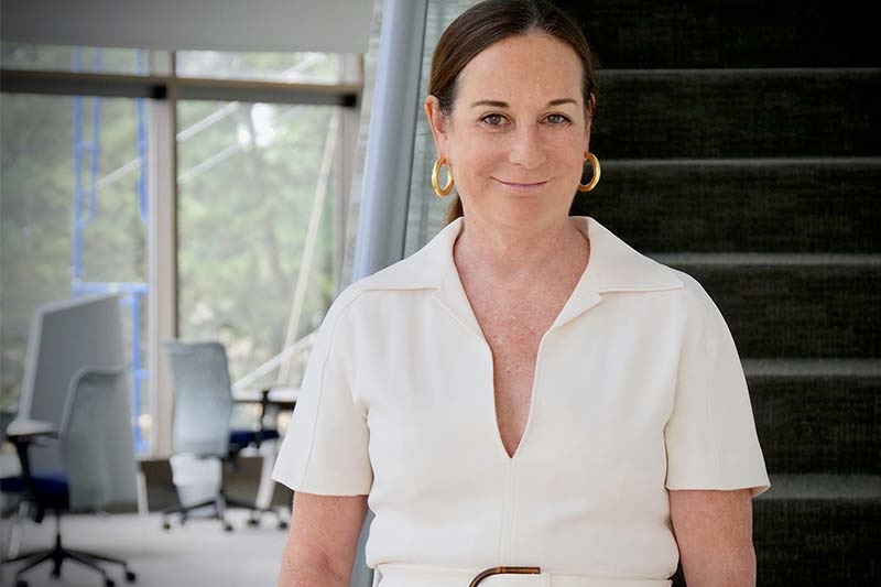 
Smiling woman in a cream v-neck shirt with gold hoop earrings, in a modern office. 
