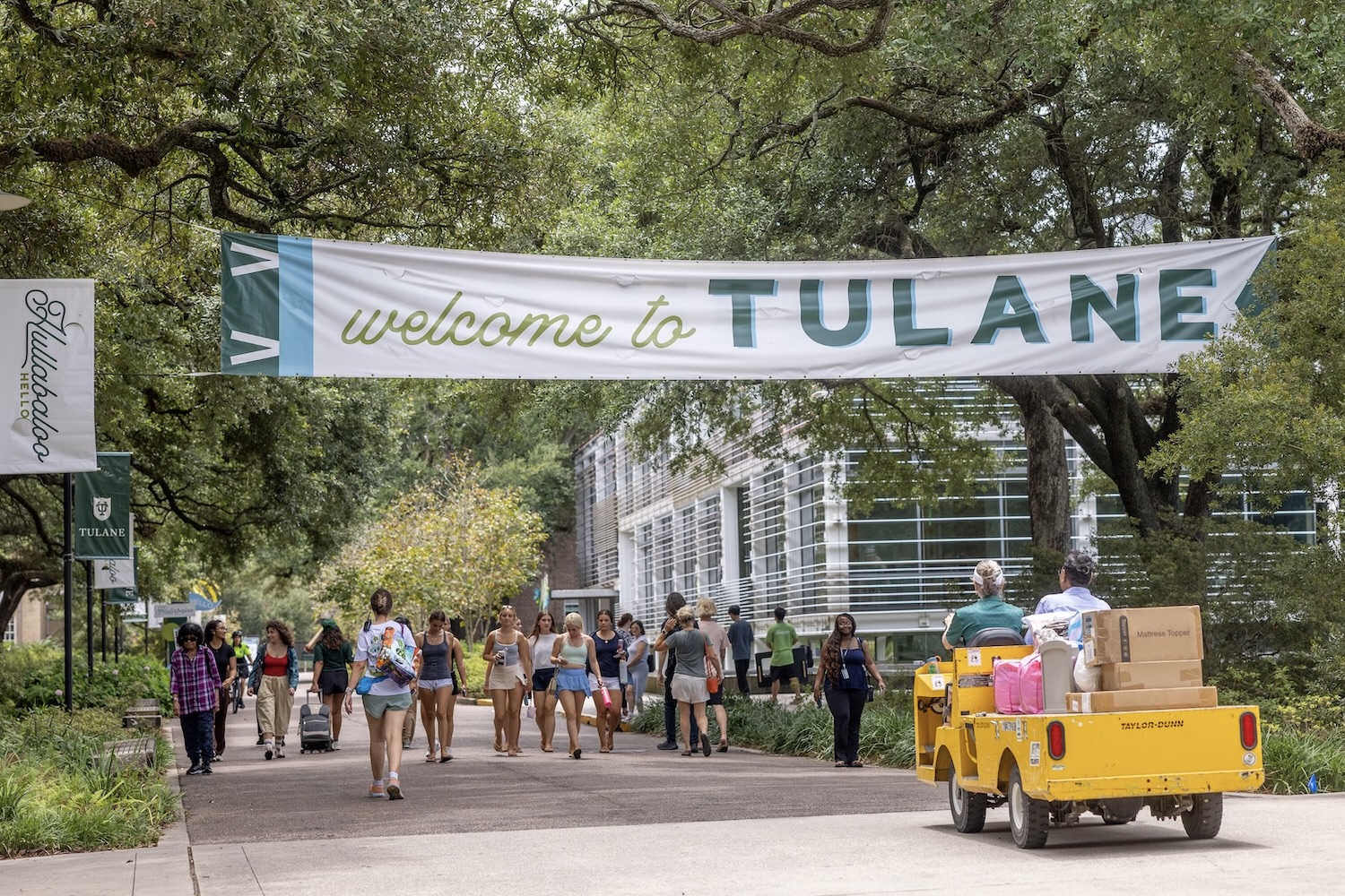 Students arrive on campus under a &amp;quot;Welcome to Tulane&amp;quot; banner; a utility cart carries luggage. 