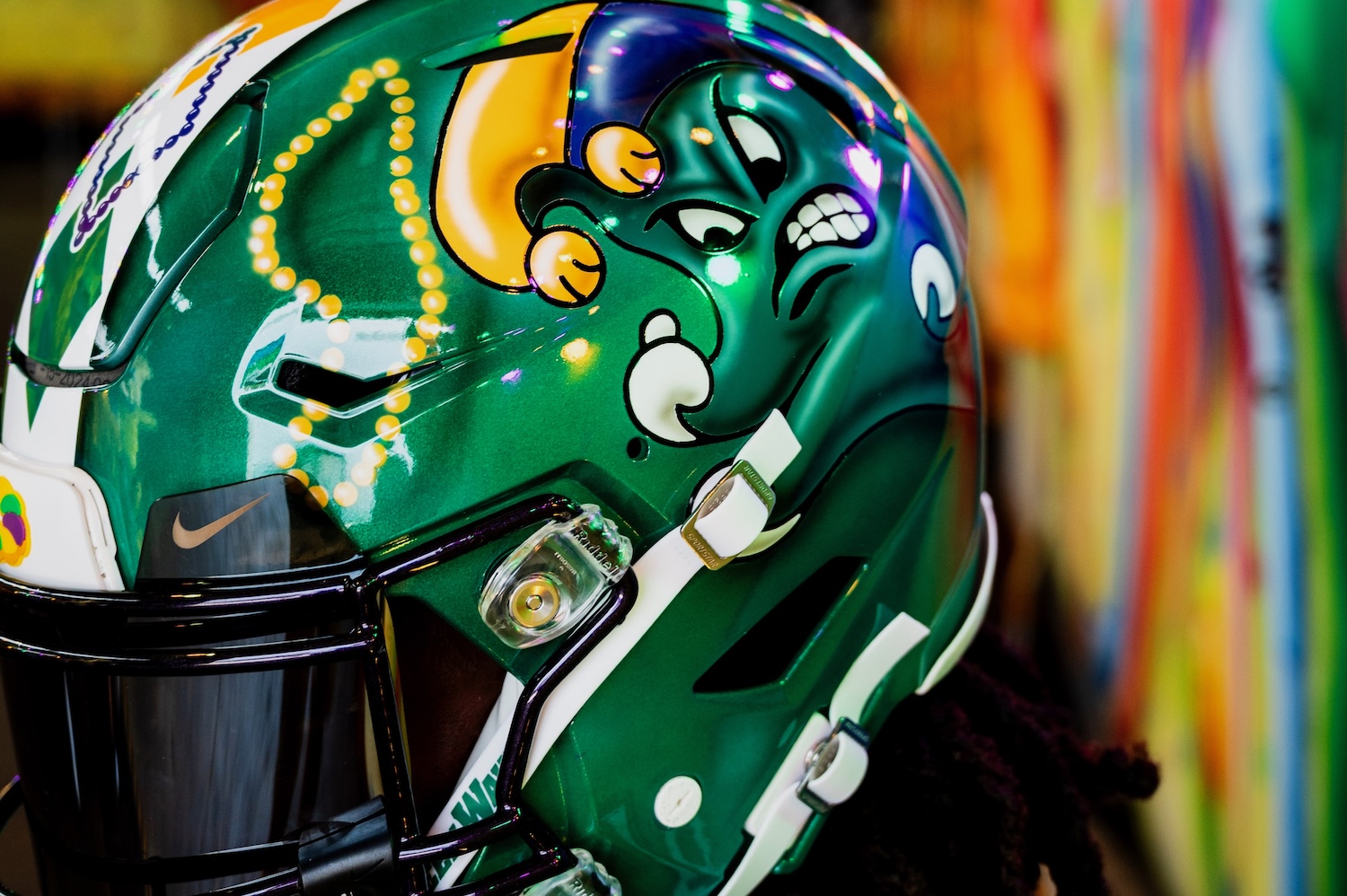 
Close-up of a green football helmet with custom Mardi Gras jester and bead designs. 