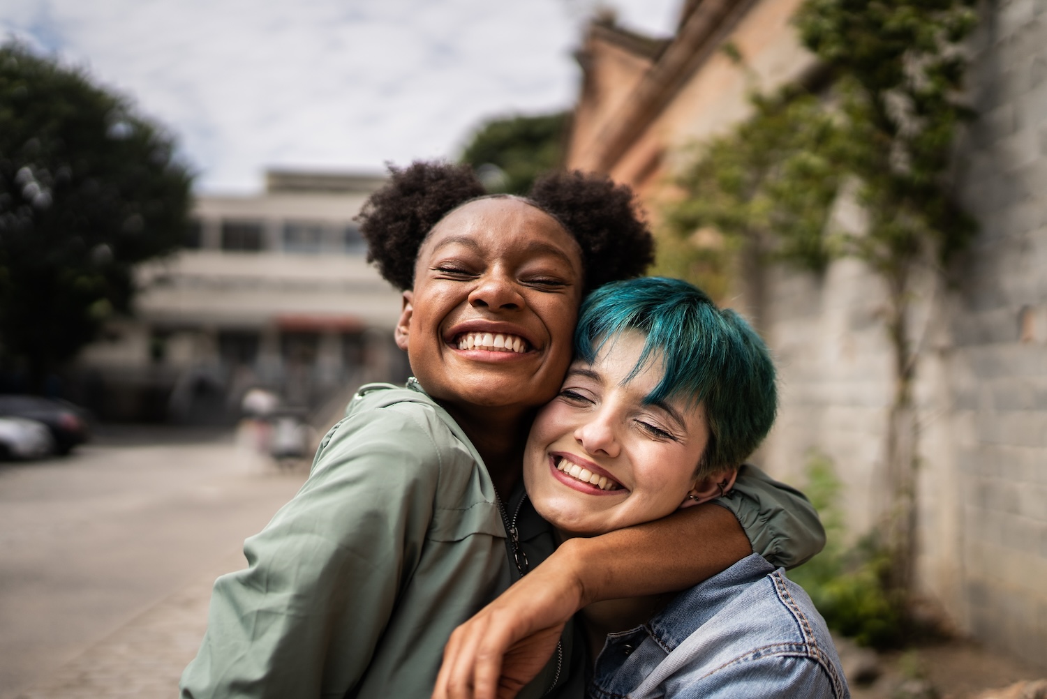 
Two happy people hugging, eyes closed, smiling broadly outdoors. 