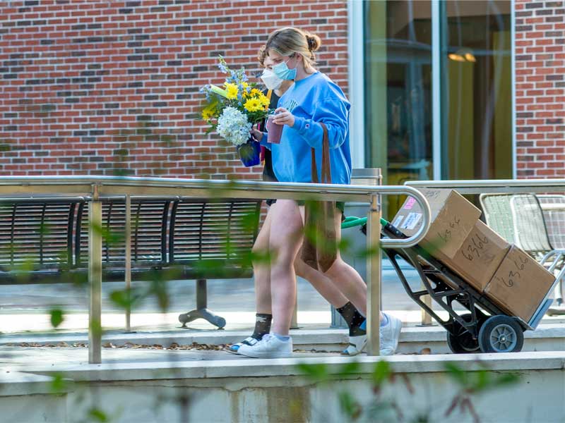 Sara Herbster carries flowers while Rosalie Kenward brings clothes that she had delivered back to her dorm room