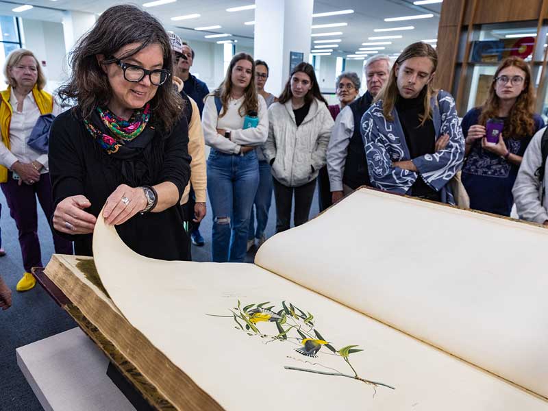 Agnieszka Czeblakow, head of research services at Tulane University Special Collections, turns a page in the giant book of illustrations as students and guests look on.