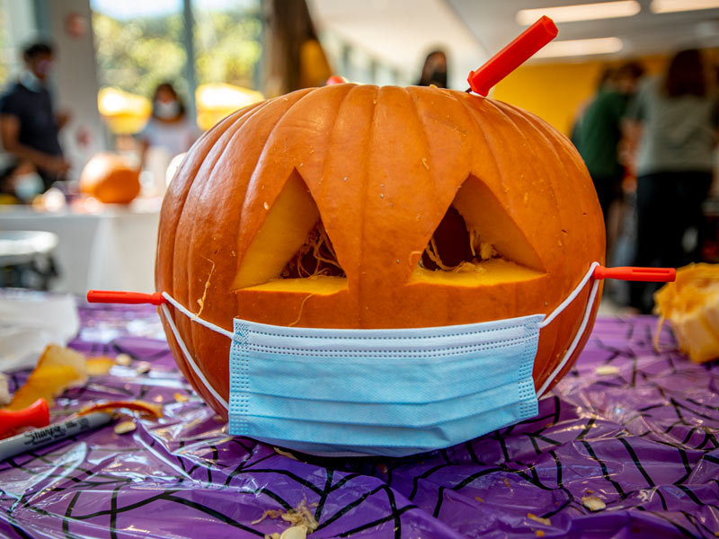 A jack-o-lantern is all smiles behind a face mask during a Global Café event where students tested their pumpkin-carving skills in Pederson Lounge in the Lavin-Bernick Center for Community Life.