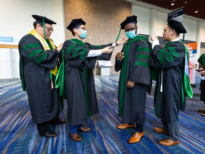 Candidates for Doctor of Medicine help each other with their regalia before the start of the 2021 School of Medicine Commencement ceremony.