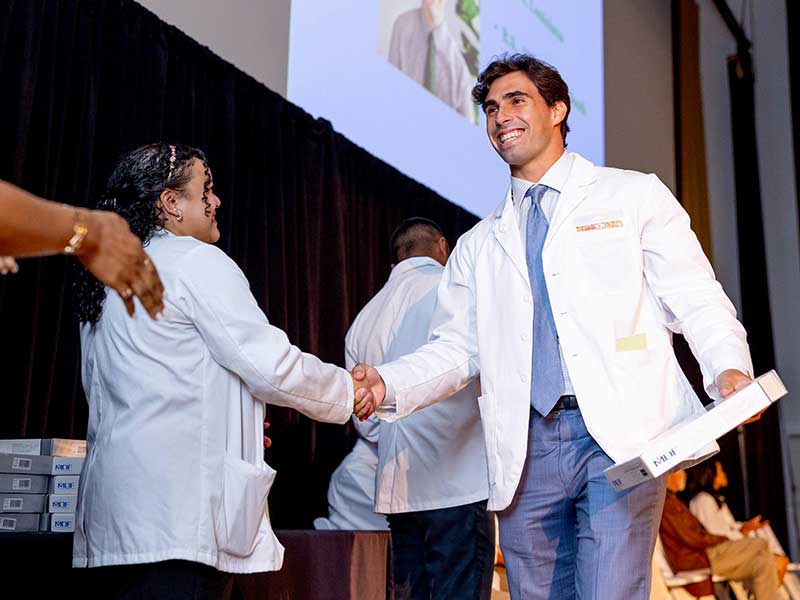 Sammy Vodovoz, student of the Class of 2027, receives his white coat and stethoscope as he crosses the stage. 