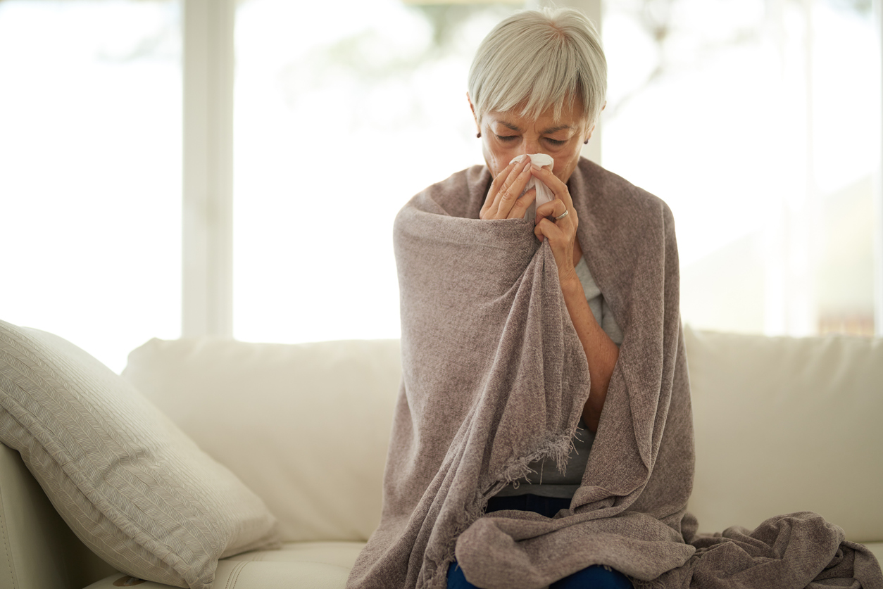 A middle-aged woman in a blanket blows her nose.
