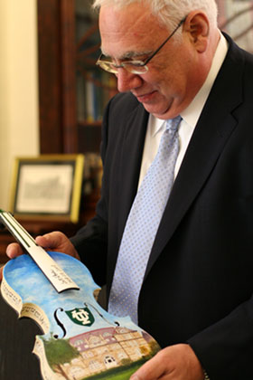 Scott Cowen holds a violin painted by researcher Ramesh Ramamoorthy.