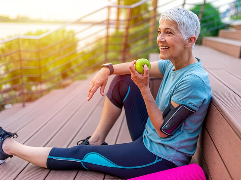 A woman in exercise clothes stops to rest and eats an apple