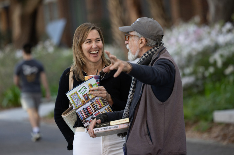 Laughing woman holds brochures while man with beard and cap points and talks.