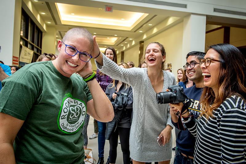 A clean-shaven Nichole Downing is all smiles as she is greeted by friends Anna Sutherland, center, Tommy John, right, and Therese Nguyen, far right. Med students go bald in support of childhood cancer research.