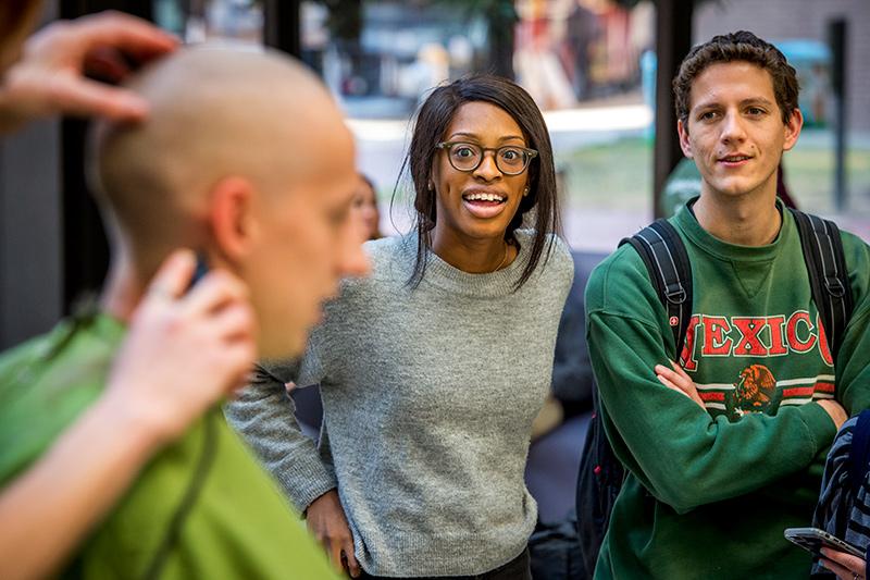 Med students Oluchi Nwosu, center, and Adam Kline watch as Quinn MacDougald succumbs to the clippers. Med students go bald in support of childhood cancer research.