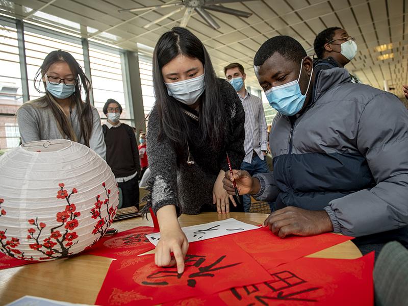 Kexin Le (left), sophomore from China, assists Emmanuel Ojah (right), a graduate student from Nigeria, as Ojah tries for the first time, the art of Chinese calligraphy.