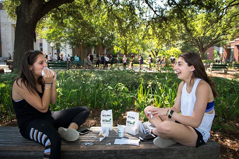 Sara Shiffman, right, laughs as Frankie Kastenbaum wipes powdered sugar from her face. The two stopped along McAlister Place to eat the beignets while still hot. Meanwhile, others wait in line for the sweet treat. Local beignet vender drives onto campus to sweeten the semester’s end.