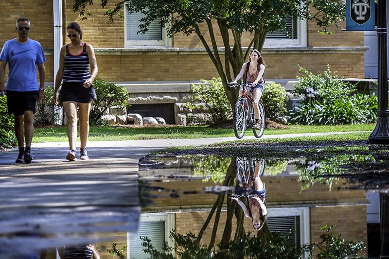  A cyclist is reflected in a puddle created by a summer rain storm near Hebert Hall on the uptown campus. 