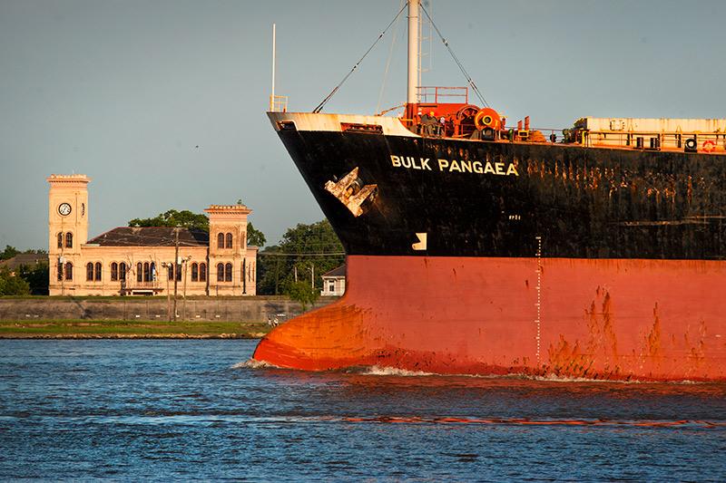 A large cargo ship heads downriver past the Algiers Courthouse.