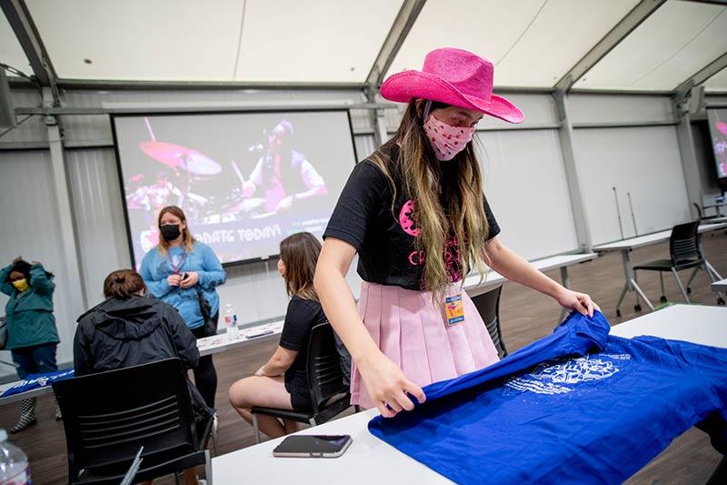 Tulane student Czars Trinidad folds a commemorative Crawfest 2021 t-shirt in the merchandise tent.