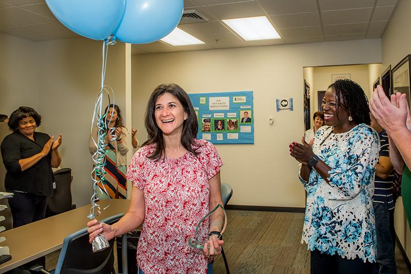 Surrounded by coworkers, Maria Villafranco, center, reacts to receiving the Tulane Spirit Award. President Fitts surprises outstanding employees with special delivery.
