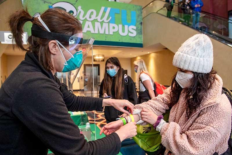 Emily Holt with Campus Health cuts off Joelle Friedman's yellow wristband after replacing it with a green one