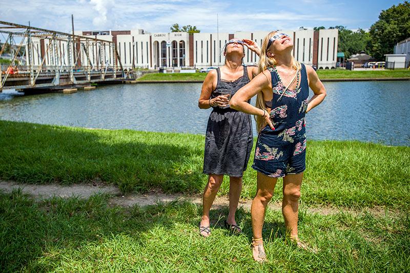 Trish Callais, left, and Michelle Roper take in the eclipse near the Cabrini Bridge on Bayou St. John. Locals are captivated by the awe-inspiring solar eclipse.