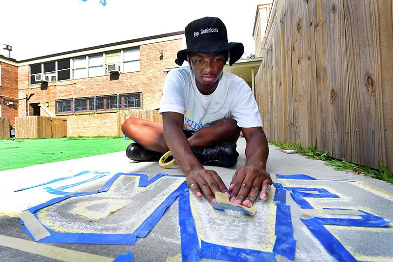 First-year student Claude Hill creates letters from tape to be spray painted at Discovery Fest on Carrollton Avenue. Students participate in the 28th annual Outreach Tulane.