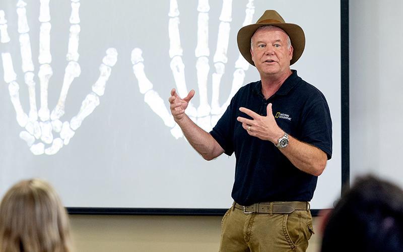 Paleoanthropologist Lee Berger in front of a photo of Homo naledi hand specimens