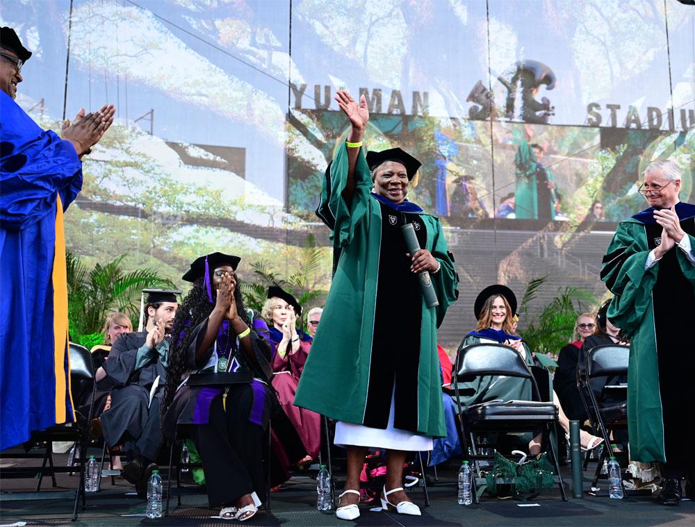 Leona Tate, civil rights activist and educator waves from the stage after bestowed an honorary degree while receiving standing ovations. Along with Tate, Dr. Victor Dzau, globally recognized physician scientist, administrator and healthcare leader, and Jon Meacham were also bestowed honorary degrees at the ceremony for their significant contributions to society. (Photo by Cheryl Gerber)