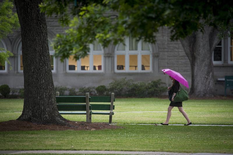 Student walks on campus with a pink umbrella