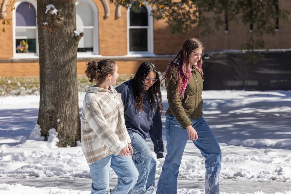 Three students walking in snow and sun