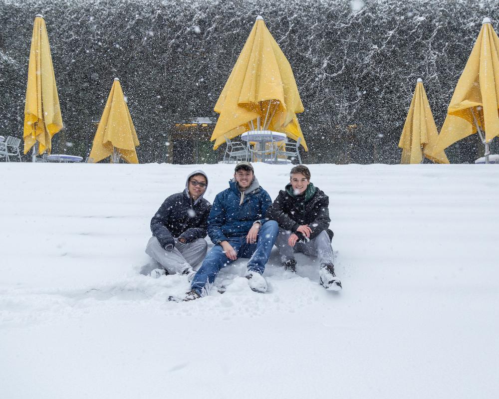 Three students posing in front of yellow umbrellas 