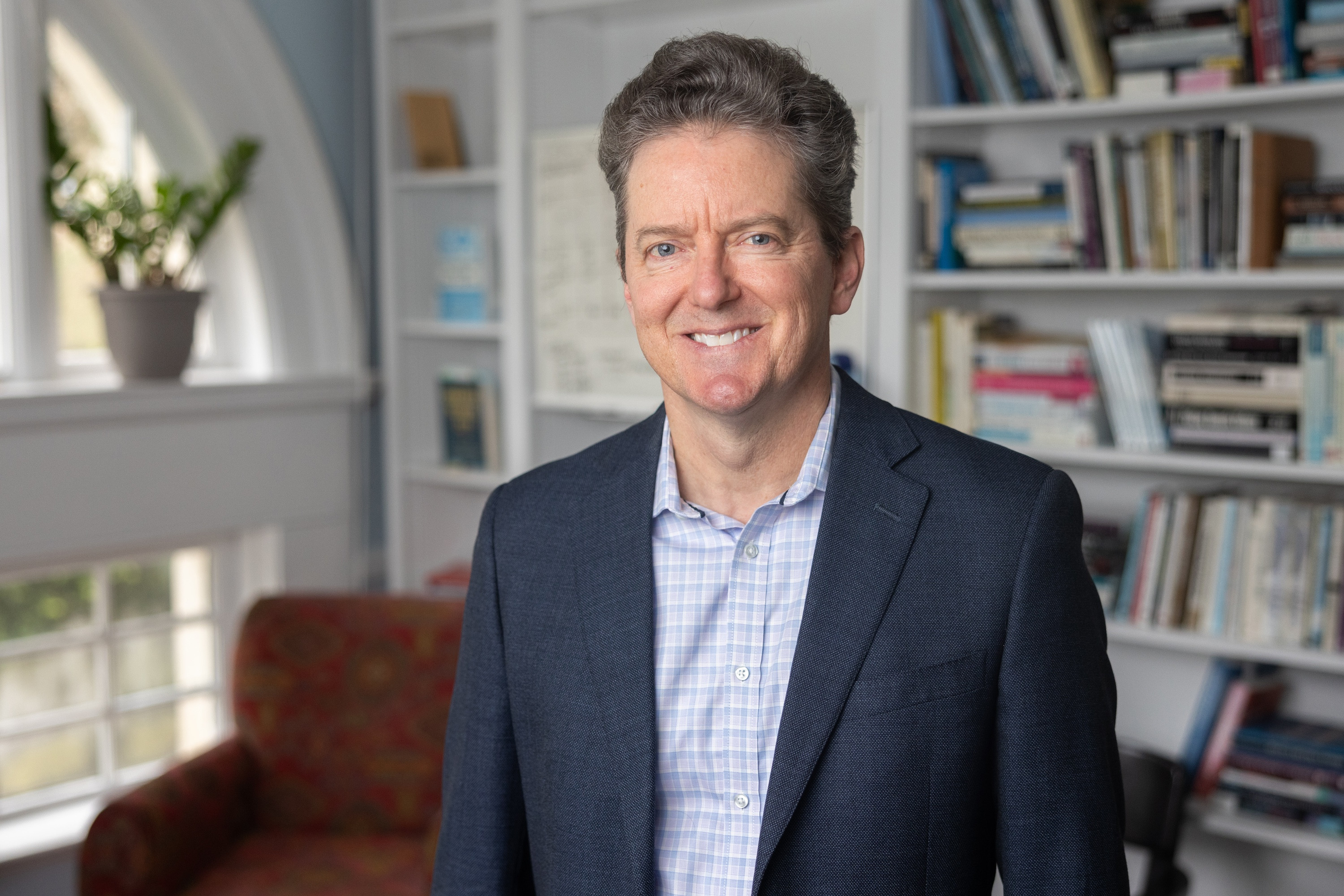 Doug Harris in blue blazer, standing in an office with a bookshelf.