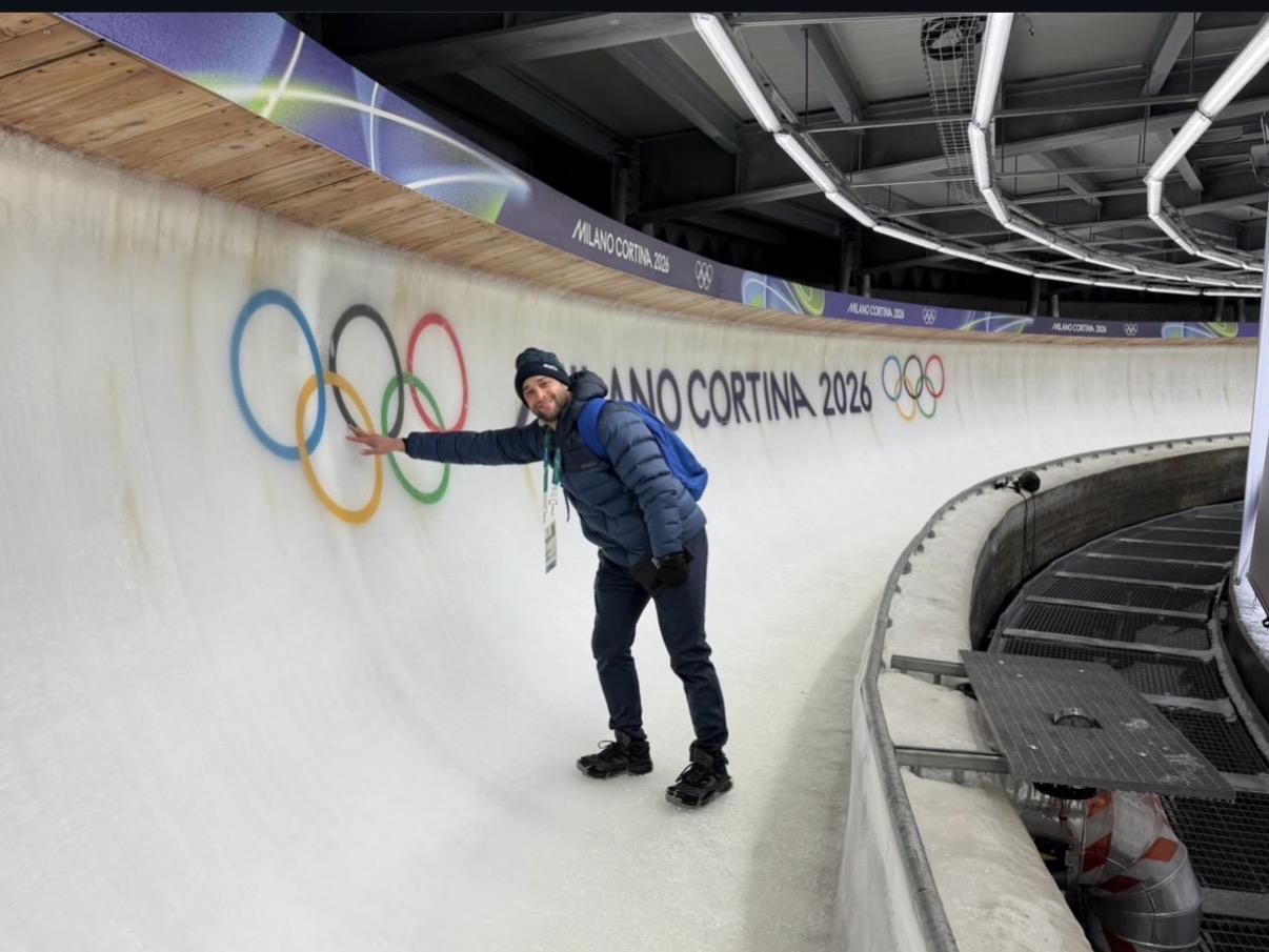 Jared Firestone touches Olympic rings on a curved ice bobsled track.