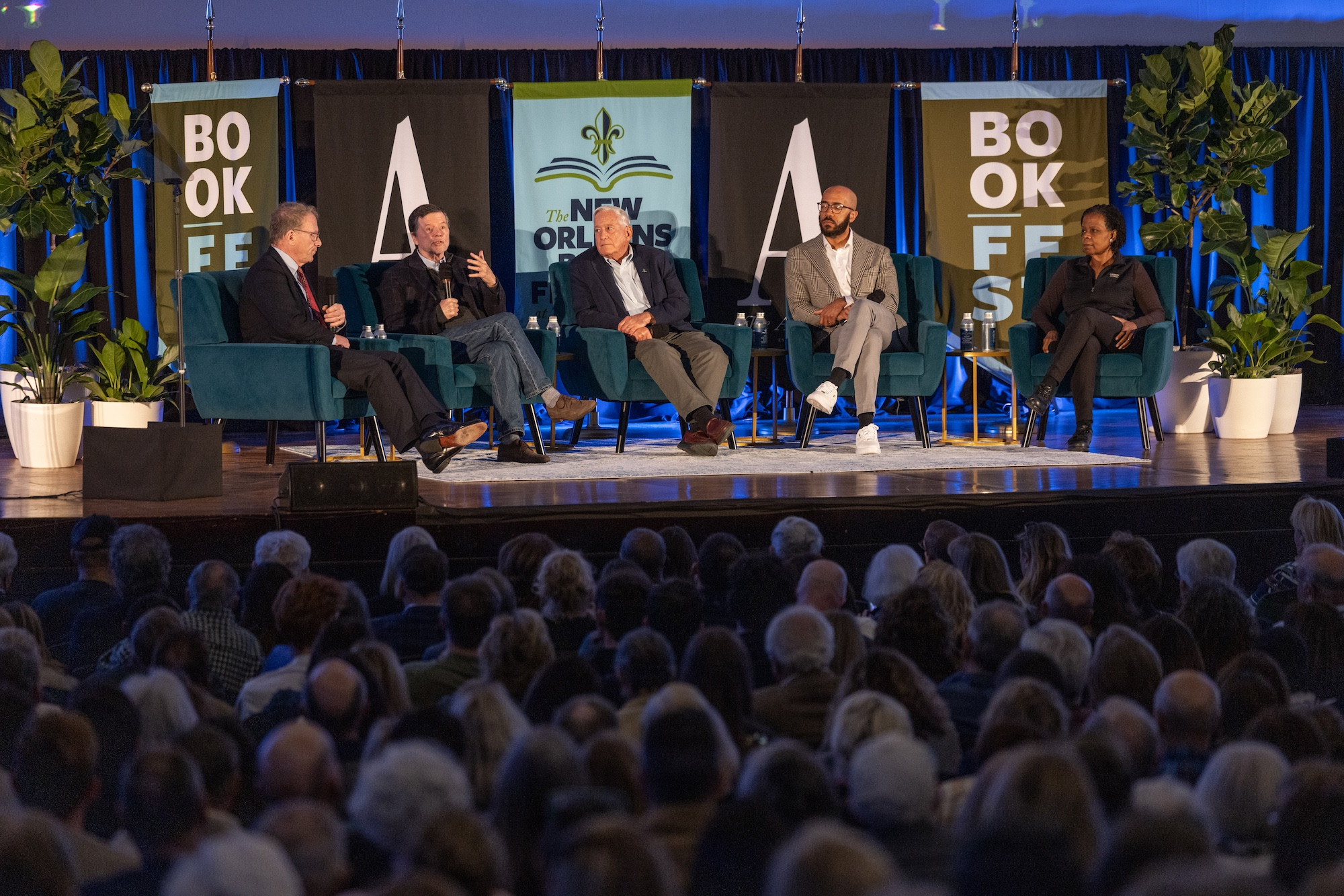 Five speakers on stage at a book festival panel, facing a large audience.