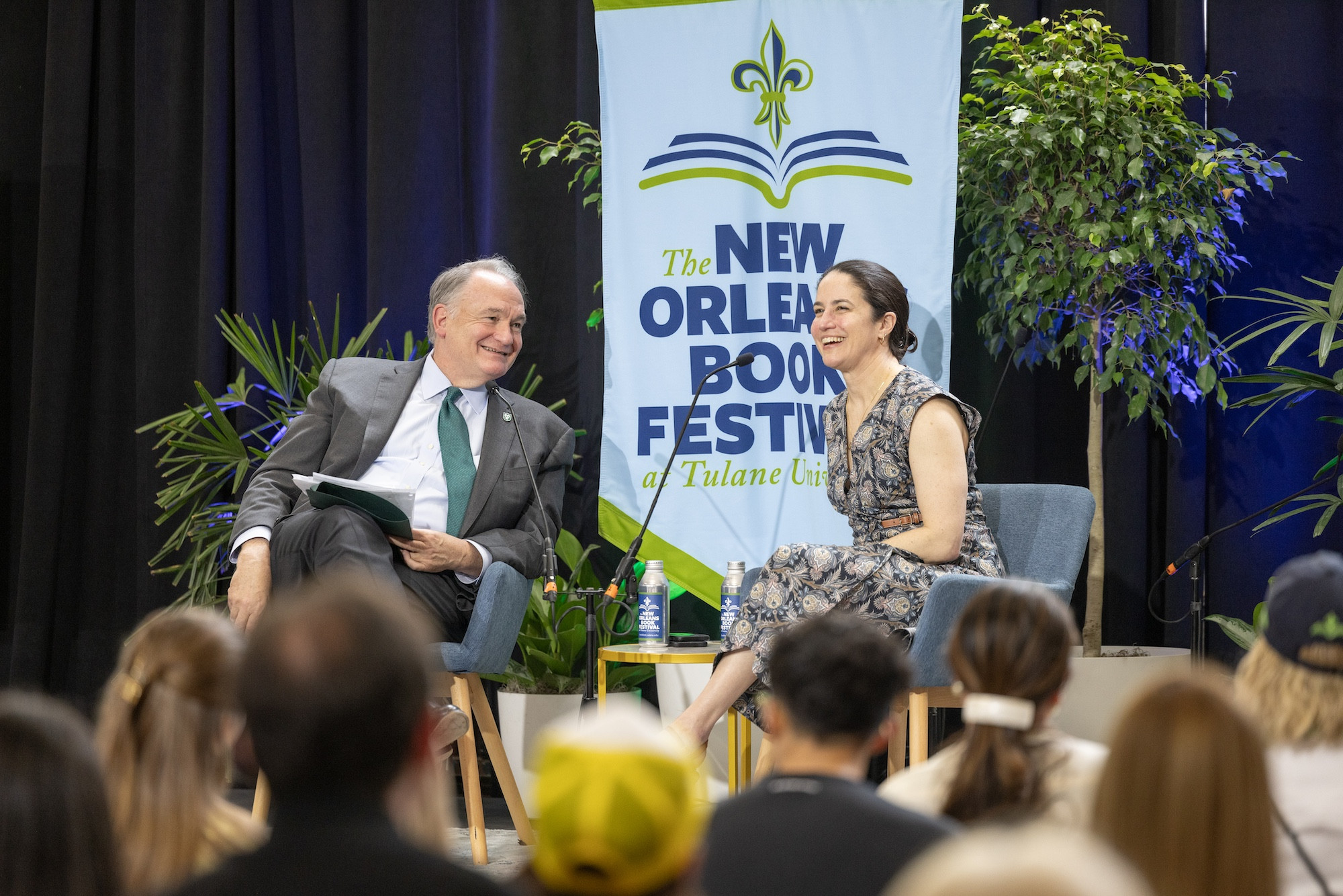 Two people smiling, talking on stage with a 'New Orleans Book Festival' banner.