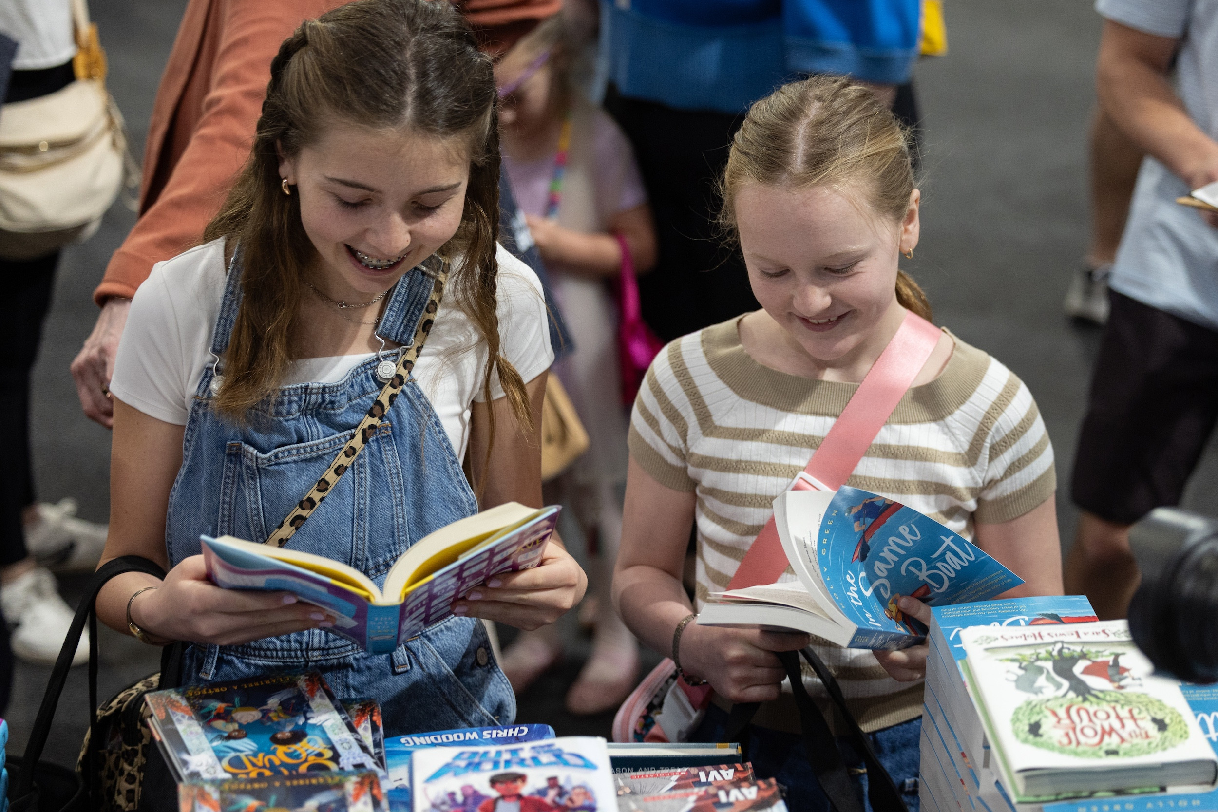 Two smiling girls read books intently, surrounded by more books on display.