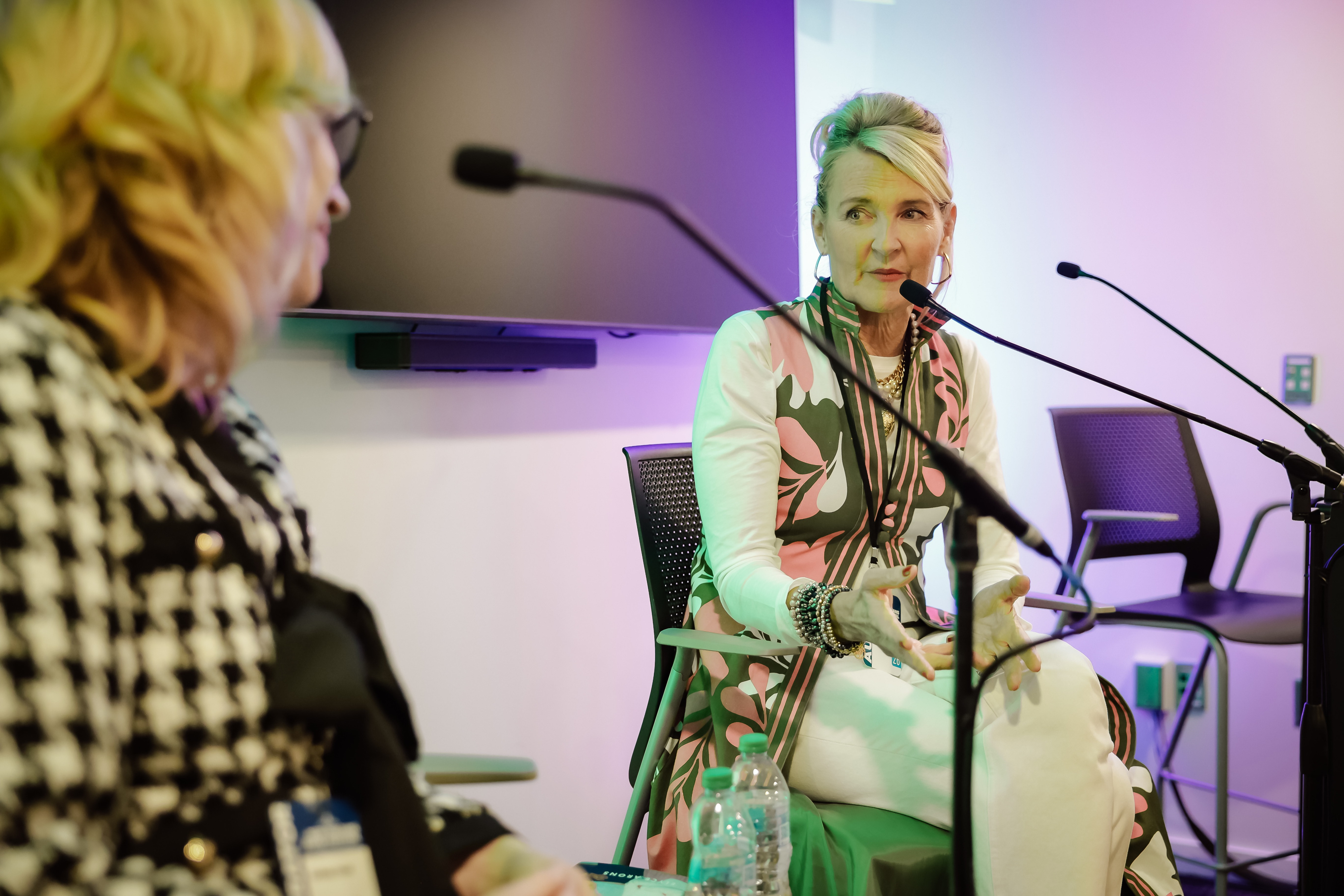 Two women on a panel, Elyse Arons speaking and gesturing while facing the Lindsay Cronk.