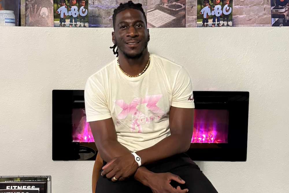 Xavier Rush in a light t-shirt sitting by a modern fireplace with purple flames.