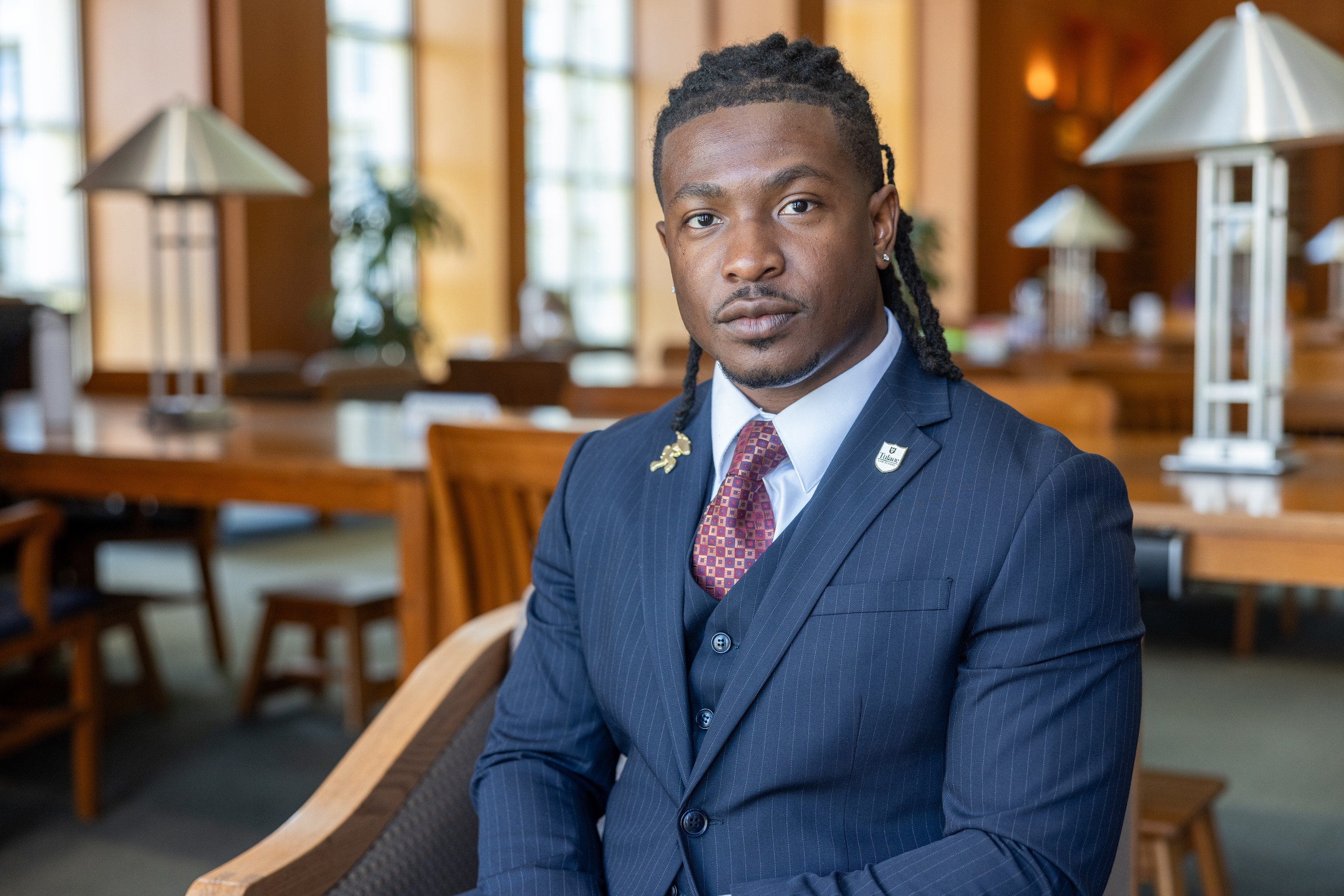 Man with dreadlocks in a suit and tie, looking at the camera, in a library.