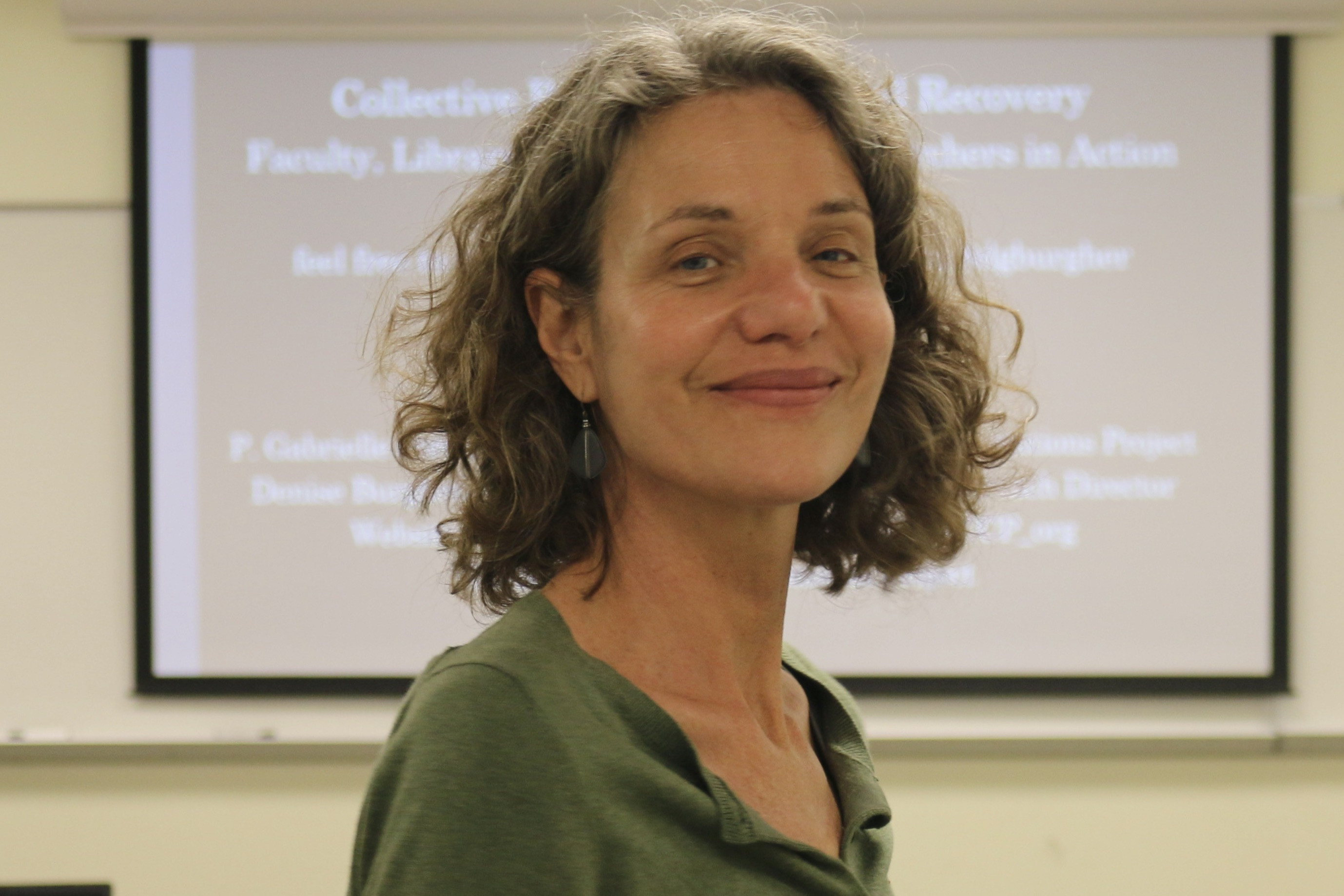 Smiling woman with curly hair wearing a green shirt, indoors.