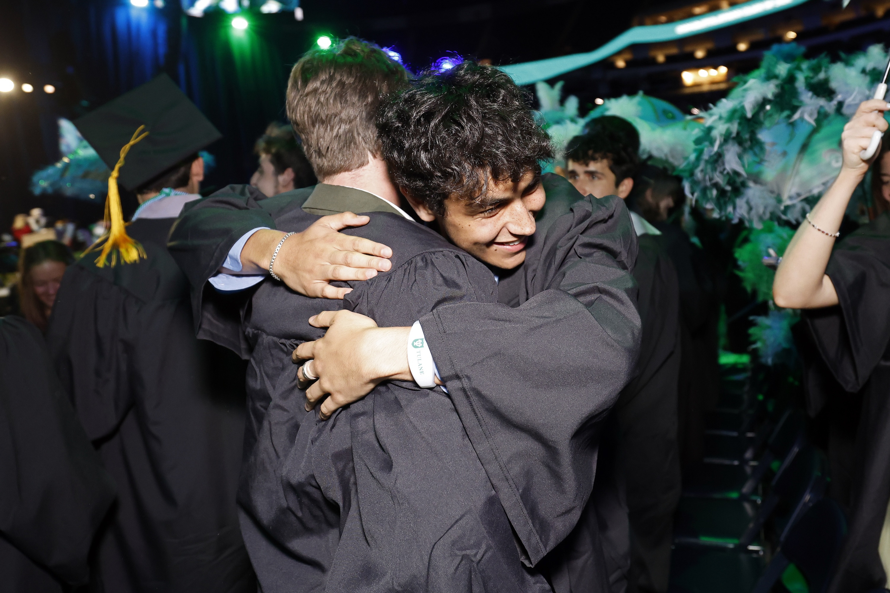 Two smiling graduates hug each other warmly at a ceremony.