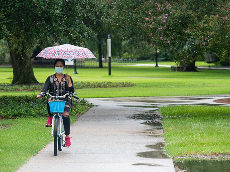 A student rides a bike on the uptown campus in the rain. 