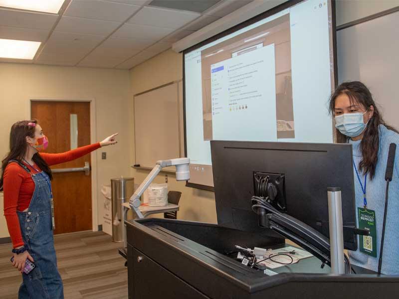Classroom Experience Assistants Anna Maija and Ansen Shen check computers in a classroom Classroom Experience Assistants Anna Maija and Ansen Shen check computers in a classroom