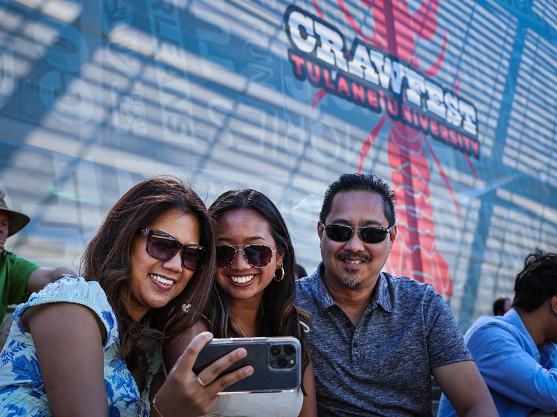 2nd year student, Alyssa Oliva, center, takes a selfie with her parents Rowena Oliva, left, and Allan Oliva, in front of the Crawfest Banner.