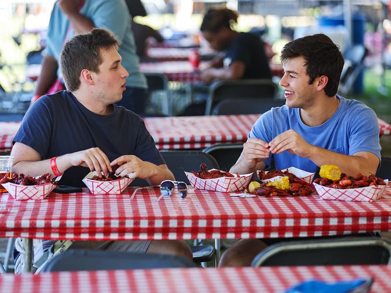 3rd year students Dylan Wolf and Zack Weinstock enjoy crawfish and a laugh in the shade of a tent on the Berger Family Lawn.